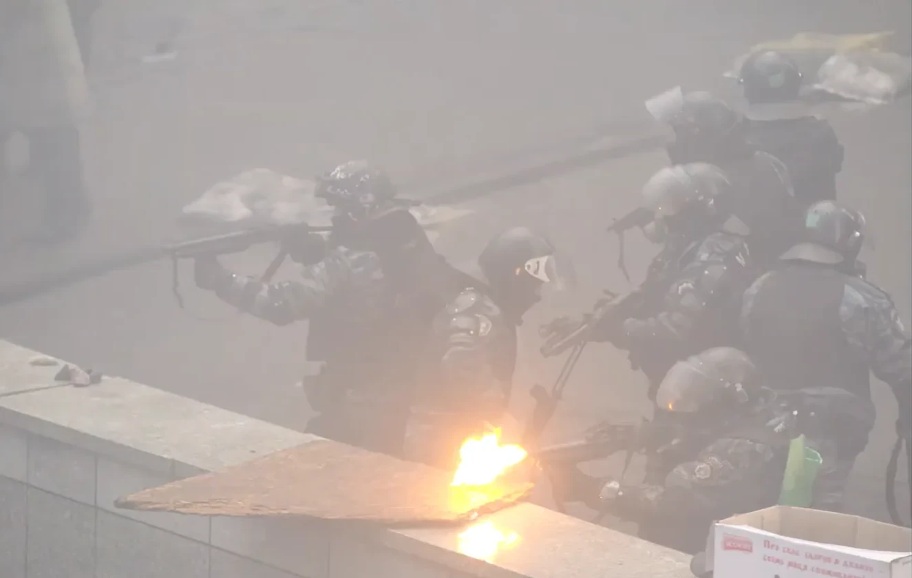 Officers in helmets with green markings fire from behind a granite parapet; a muzzle flash