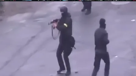 An officer in black with a rifle and a yellow armband on his sleeve
