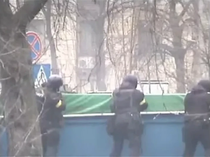 Officers with armbands on their sleeves behind the blue body of a truck at the concrete barricade